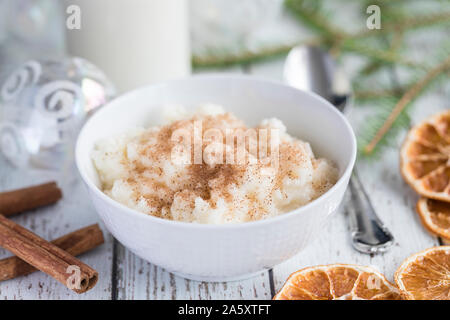 Tradizionale budino di riso noto anche come tomtegröt o risgrynsgröt svedese. Il budino di riso è in un colore bianco porcellana ciotola su una bianca tavolo in legno con Foto Stock