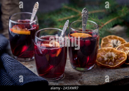 Vin brulé con bastoncini di cannella, secchi Arance e mirtilli rossi. I bicchieri sono su una pietra calcarea con lo sfondo di un verde di pini ramo di albero nella parte posteriore Foto Stock