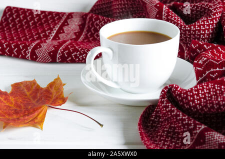 Un bianco rotondo tazza e piattino sorge su un bianco tavolo di legno accanto ai libri gialli e foglie di autunno Foto Stock