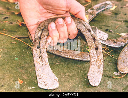 Mano pick up argento usato ferri di cavallo da terra punteggiata di foglie cadute. Caduta stagione a cavallo fattoria gamma. Foto Stock