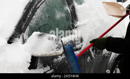 L'uomo cancella auto da neve in una fredda giornata invernale dopo la nevicata. Spazzola in mano mans. Tanta neve su auto. Foto Stock