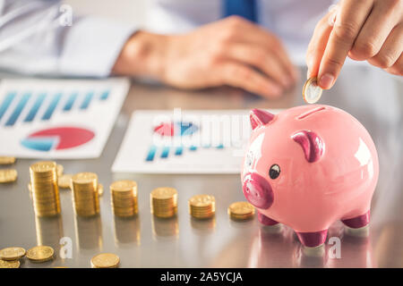 Banchiere commercialista o assicuratore mettere soldi in un salvadanaio. Tabella finanziaria da monete concetto aziendale Foto Stock