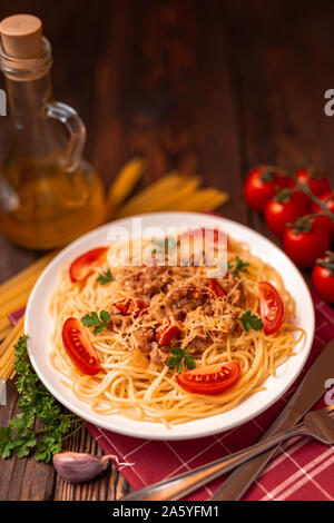 Pasta bolognese con salsa di pomodoro e carne macinata, parmigiano grattugiato e prezzemolo fresco - le sane pasta italiana su sfondo rustico Foto Stock