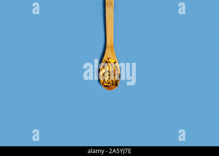 Concetto di dieta. Isolato sfondo blu con olio di pesce capsule sul cucchiaio di legno nel centro di un'immagine. Appartamento laico, vista dall'alto. Foto Stock