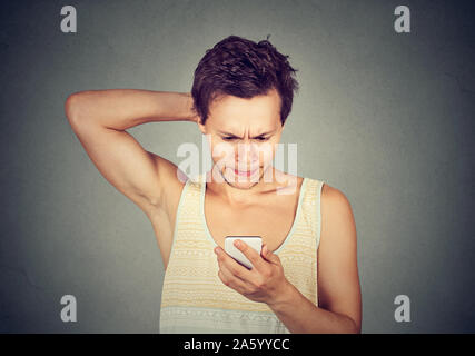 Ritratto di un giovane uomo che guarda un telefono cellulare con espressione confusa sul viso Foto Stock