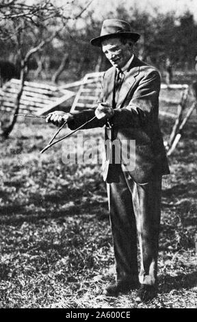 Acqua rabdomante serranda o utilizzando un ramoscello a forcella; 1930. Radioestesia è un tipo di divinazione impiegato nel tentativo di individuare acqua macinata, sepolto metalli o minerali, gemme, olio, gravesites e molti altri oggetti e materiali senza l'uso di apparecchi scientifici Foto Stock