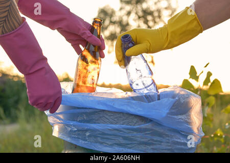 Giovani amici di porpora e giallo guanti di gomma sono a piedi con sacchi della spazzatura lungo una zona verde di una spiaggia sporca del fiume e la pulizia di lettiera Foto Stock