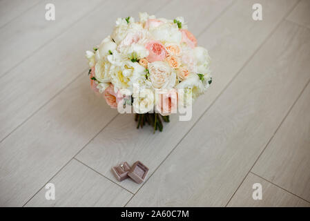 Bouquet nozze giacente sul tappeto grigio durante la preparazione prima della celebrazione. Vista laterale del decoro rose,le peonie fiori e foglie bouquet. Foto Stock