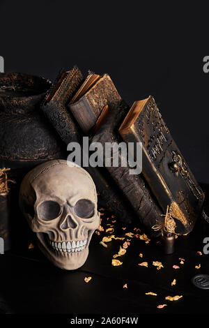 Modello realistico di un cranio umano con denti bianchi, vecchia pentola, libri con incantesimi e vasetti di pozione sono su una tavola di legno tabella scuro. Petali di essiccato ros Foto Stock