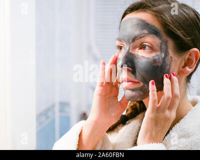 La ragazza si prende cura per la pelle grassa. Procedure cosmetiche. La cura della pelle. Giovane donna con un nero maschera di fango sul suo viso. pulizia pori. Procedure cosmetiche. Foto Stock