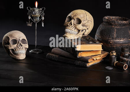 Modello realistico di due craniums umana con denti bianchi, libri con incantesimi, vecchia pentola, vasi di pozione, candela che brucia nel candelabro sono in legno scuro Foto Stock