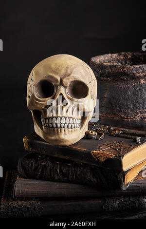 Modello realistico di un teschio umano con denti su un vecchio libri contro un recipiente scuro. Sfondo nero. La scienza medica o di Halloween concetto di orrore. Magic, Foto Stock