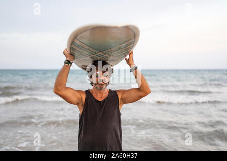 Ritratto di uomo maturo che trasportano le tavole da surf al mare Foto Stock