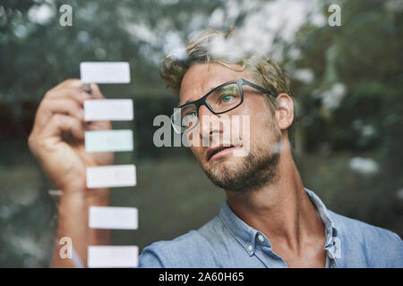 Casual giovane imprenditore con note adesive dietro il vetro di finestra di office Foto Stock