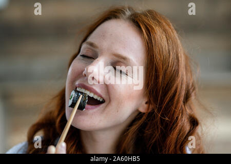 Ritratto di felice redheaded donna mangiare sushi Foto Stock