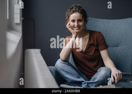 Ritratto di giovane sorridente donna seduta sulla poltrona di casa Foto Stock