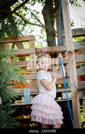 Ragazza vestita come una principessa con corona e scettro giocando in un albero di casa Foto Stock