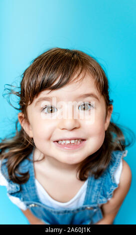 Ritratto di incantevole piccola ragazza sorridente molto espressivo su sfondo blu Foto Stock