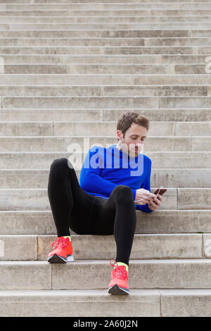 Seduta del pareggiatore sui gradini e utilizza lo smartphone Foto Stock