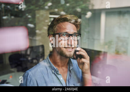 Casual giovane uomo d affari al telefono dietro il vetro di finestra di office Foto Stock