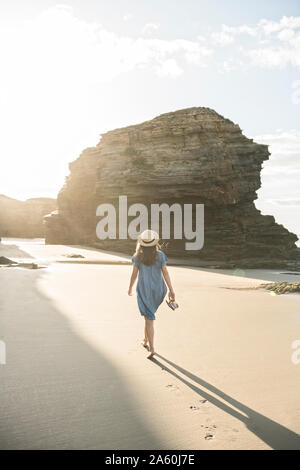 Donna che cammina sulla spiaggia con rocce, vista posteriore Foto Stock