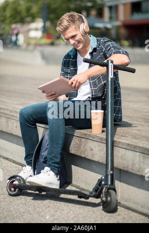 Giovane uomo con e-scooter utilizzando tablet in città Foto Stock