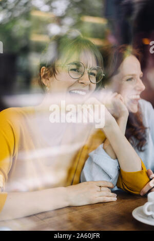 Due happy amici di sesso femminile dietro il vetro di finestra in un cafe Foto Stock