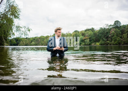 Imprenditore in piedi in un lago con un telefono cellulare Foto Stock
