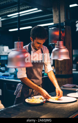 Lo chef serve pasti su piatti nella cucina di un ristorante Foto Stock