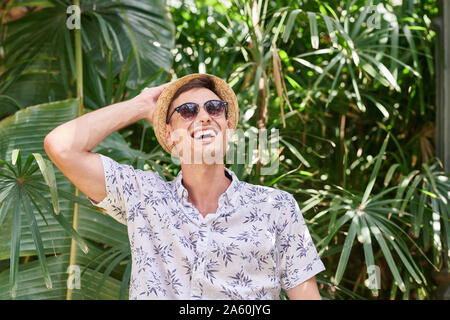 Uomo sorridente con il cappello e occhiali da sole in un parco Foto Stock