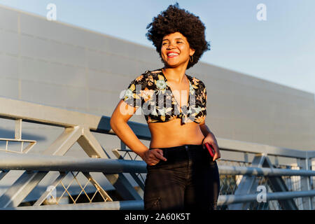 Sorridente donna Afroamericana con smartphone rosso cercando lateralmente Foto Stock