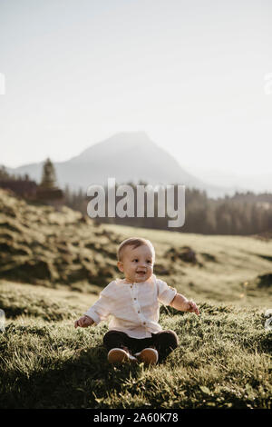 Felice piccolo ragazzo seduto su un prato alpino, Schwaegalp, Nesslau, Svizzera Foto Stock