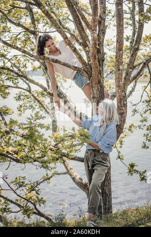 Madre guarda la figlia, arrampicata in una struttura ad albero Foto Stock