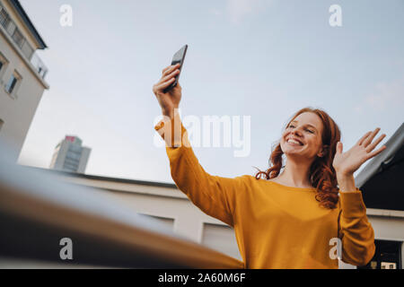 Sorridente donna redheaded tramite telefono cellulare sulla terrazza sul tetto Foto Stock