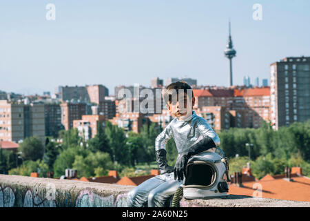 Ritratto di ragazzo vestito come un astronauta seduto su una parete in città Foto Stock