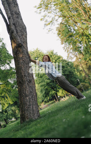 La donna in un parco spingendo inclinato trree tronco Foto Stock