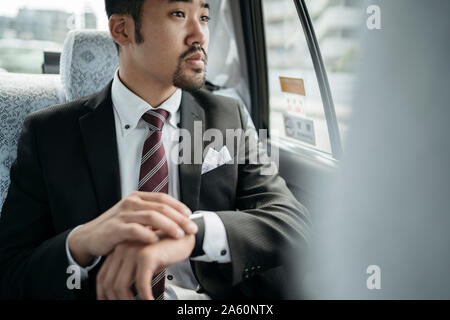 Giovane imprenditore in un taxi controllando il tempo e guardando fuori della finestra Foto Stock