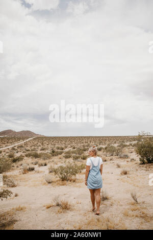 Giovane donna a piedi attraverso il paesaggio del deserto, Joshua Tree National Park, California, Stati Uniti d'America Foto Stock