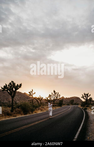 Donna che cammina sulla strada al tramonto, Joshua Tree National Park, California, Stati Uniti d'America Foto Stock