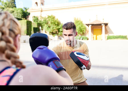 Fitness coach praticando la boxe con classe giovane donna all'aperto nella città Foto Stock