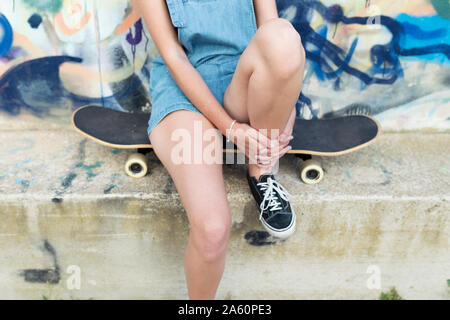 Giovane donna seduta su skateboard in parte anteriore del graffiti Foto Stock