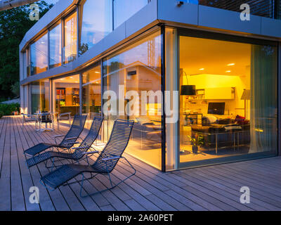 Svizzera, tre sedie a sdraio sulla terrazza illuminata di moderna villa al crepuscolo Foto Stock