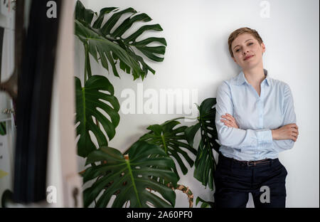 Ritratto di un fiducioso imprenditrice sta in piedi in una parete accanto a un impianto Foto Stock