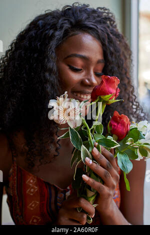 Ritratto di giovane donna africana profumati fiori e sorridente in un cafe Foto Stock