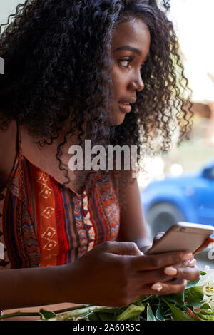 Ritratto di giovane donna africana in un cafe, controllando il suo smartphone