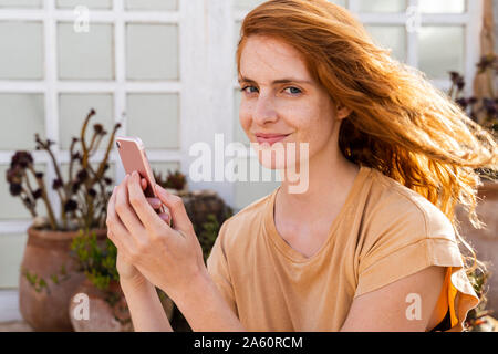 Ritratto di redheaded sorridente giovane donna con lo smartphone sulla terrazza Foto Stock