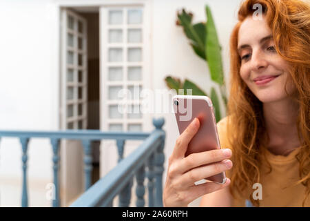 La mano di sorridere redheaded giovane donna azienda telefono cellulare, close-up Foto Stock