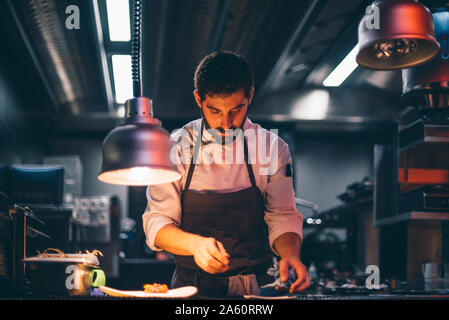 Lo chef serve pasti su piatti nella cucina di un ristorante Foto Stock