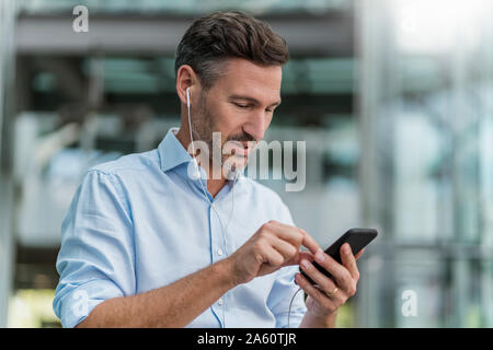 Imprenditore con auricolari e telefono cellulare nella città Foto Stock