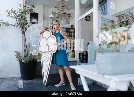 La donna in piedi di fronte a lei coffee shop, tenendo icecream segno Foto Stock